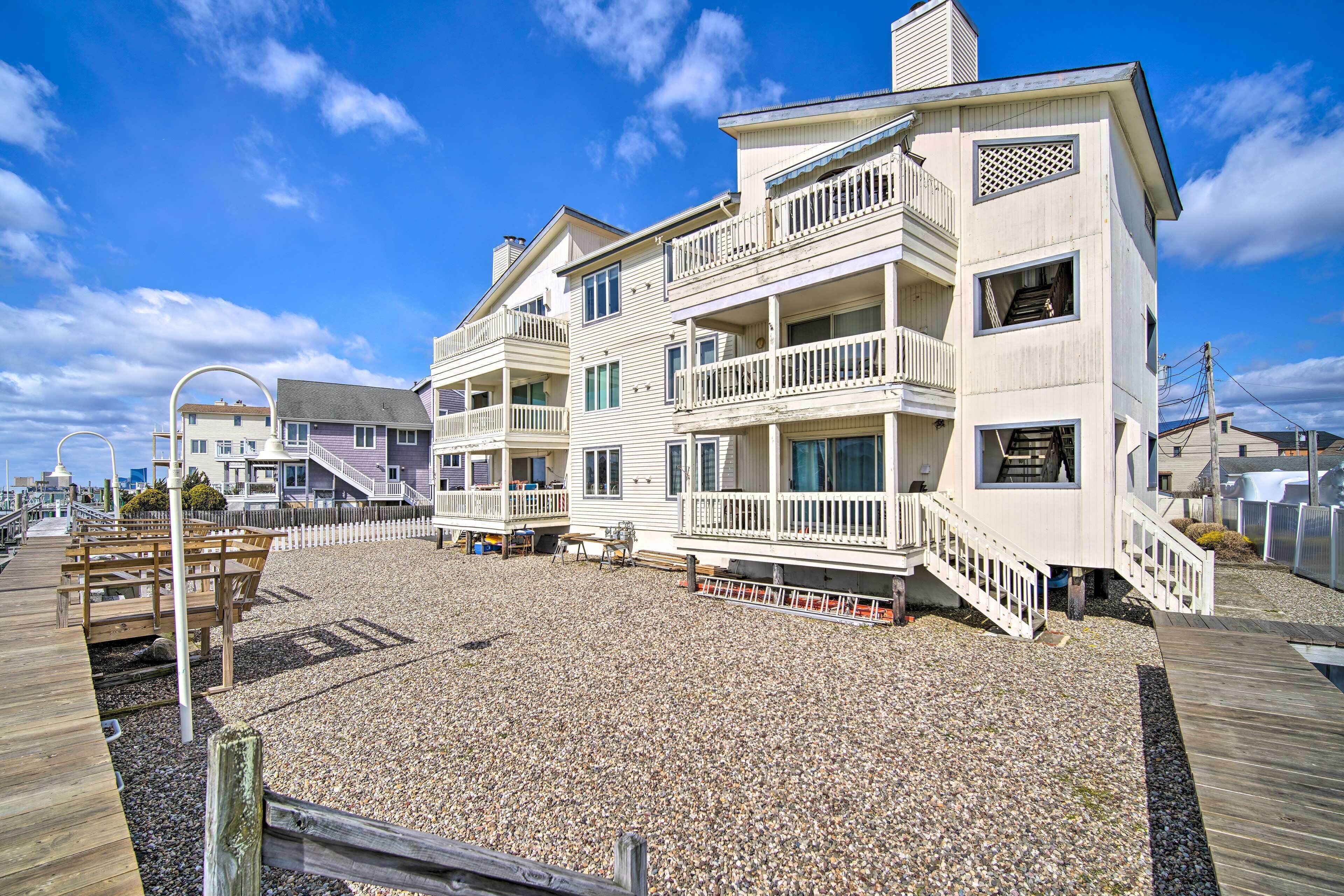 Un edificio frente a la playa con varios pisos, balcones, una terraza de madera y una escalera que sube a los niveles superiores.