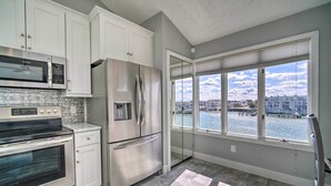 A modern kitchen with stainless steel appliances, white cabinetry, and a large window overlooking a waterfront.