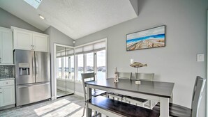 A modern kitchen with a stainless steel refrigerator, white cabinets, and a dining area with a dark wooden table and white chairs.