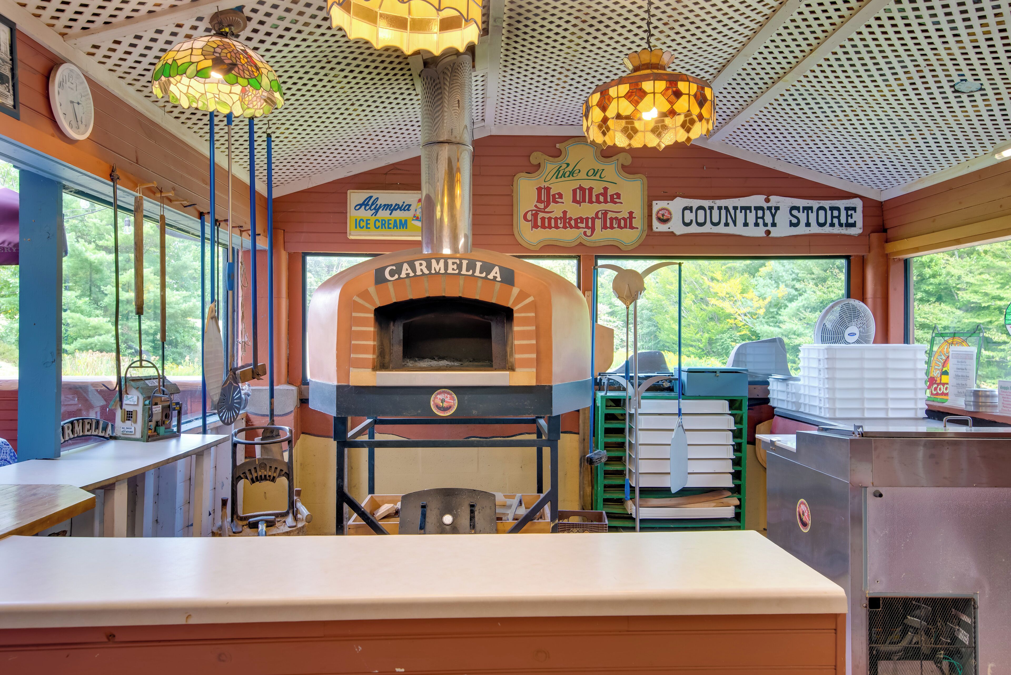 A rustic interior with a brick oven labeled 'Carmella', a 'Country Store' sign, and a 'Ride on Ye Olde Turkey Town' sign.