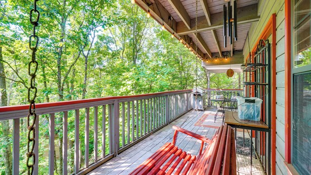 A wooden deck with a red bench, a table with a chair, and a hanging light fixture.