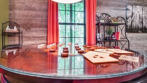 A round glass table with tea sets and teapots, a wooden wall, and a window with red curtains.
