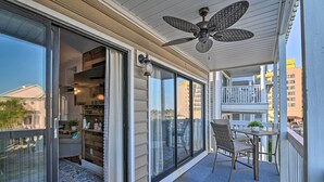 A balcony with a ceiling fan, a table with chairs, and a sliding glass door leading to an interior space. - Eclectic Condo w/ Balcony: 1 Block to Beach! (Surfside Beach)