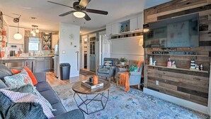 A modern living room with a sofa, coffee table, and a television mounted on a wooden wall. - Eclectic Condo w/ Balcony: 1 Block to Beach! (Surfside Beach)