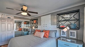 A bedroom with a bed, a ceiling fan, a dresser, and a wall with framed pictures and a shelf with decorative items. - Eclectic Condo w/ Balcony: 1 Block to Beach! (Surfside Beach)