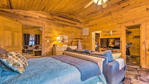 Un dormitorio tipo cabaña de madera con una cama grande, un sofá, un televisor y un ventilador de techo.