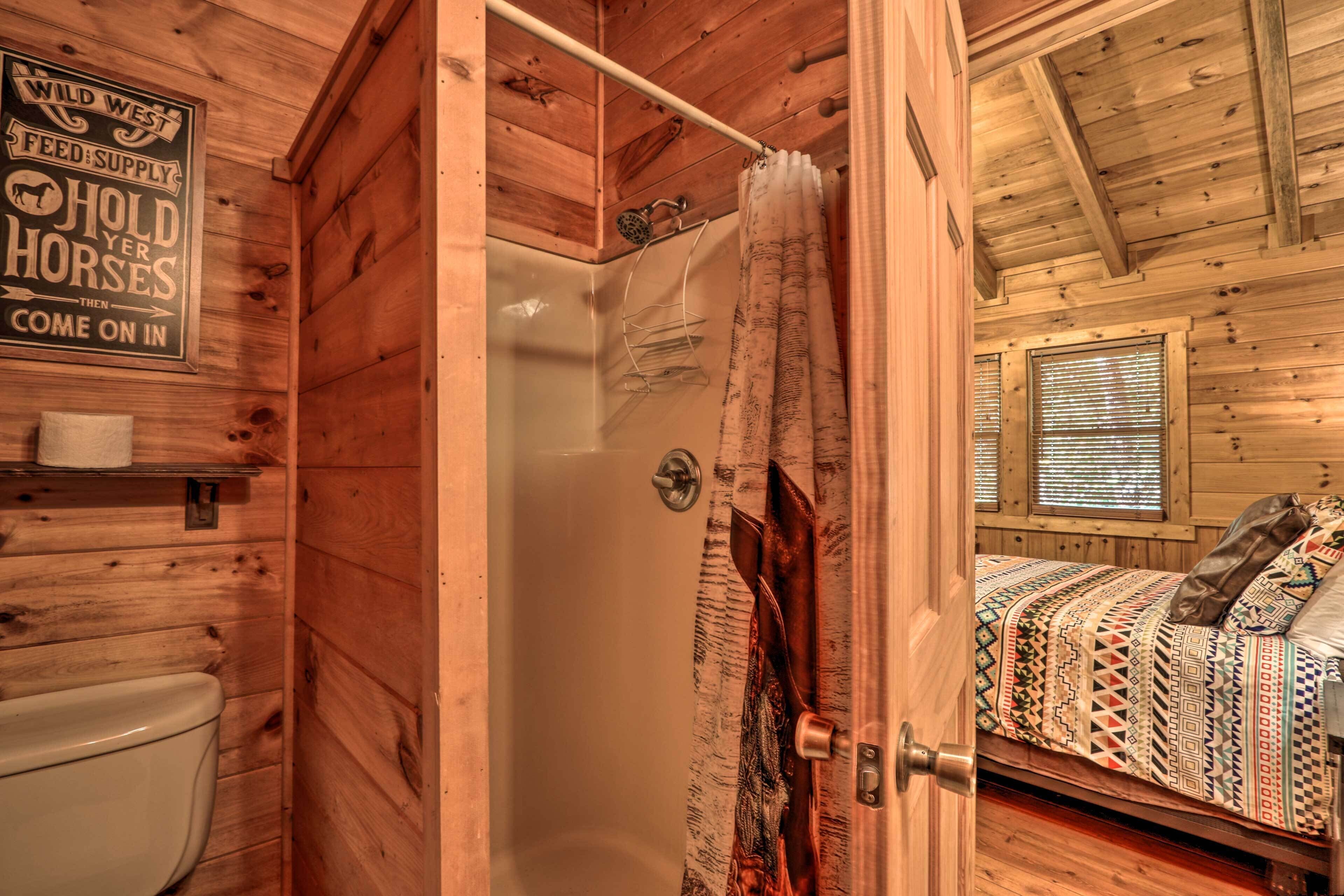 Interior de cabana de madeira com chuveiro, cama com roupa de cama estampada e um letreiro na parede.