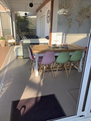 Un coin repas avec une table en bois et des chaises colorées, une carte accrochée au mur et une vue sur l’extérieur.