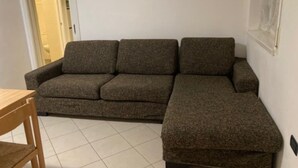 A corner room with a brown sofa, a wooden chair, and a tiled floor. - house-parking-wifi-adige muse (Trento)