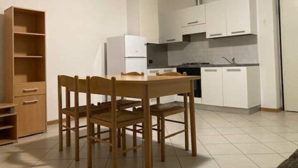 A compact kitchen with white cabinets, a white refrigerator, a stove, and a dining table with chairs. - house-parking-wifi-adige muse (Trento)