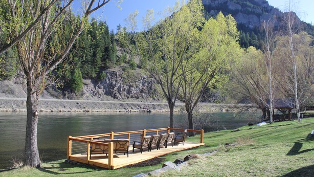 A wooden deck with chairs overlooking a river, surrounded by trees and a mountain in the background. - High End Lodging for Medium to Large Groups in the Canyon of the Missouri River! (Craig)
