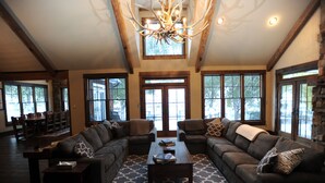 A spacious living room with a large sectional sofa, a wooden coffee table, and a patterned rug. There are multiple windows providing natural light and a view of the outdoors. - High End Lodging for Medium to Large Groups in the Canyon of the Missouri River! (Craig)
