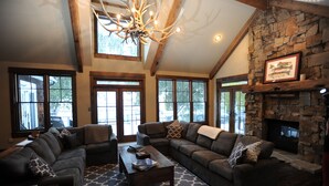A spacious living room with a stone fireplace, large windows, and a chandelier. - High End Lodging for Medium to Large Groups in the Canyon of the Missouri River! (Craig)
