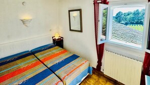 Un petit logement composé d’une seule pièce, comprenant un lit, une fenêtre donnant sur un espace verdoyant, un radiateur et un luminaire fixé au mur.
