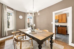 A dining room with a wooden table, chairs, a chandelier, and a view of the kitchen. - Charming DC Rowhome w/ Off-Street Parking, Metro Access & Walkable to Everything (Washington)
