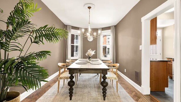Ein Esszimmer mit einem großen Tisch, Stühlen, einer Chandelüster und einem Blumentopf.
