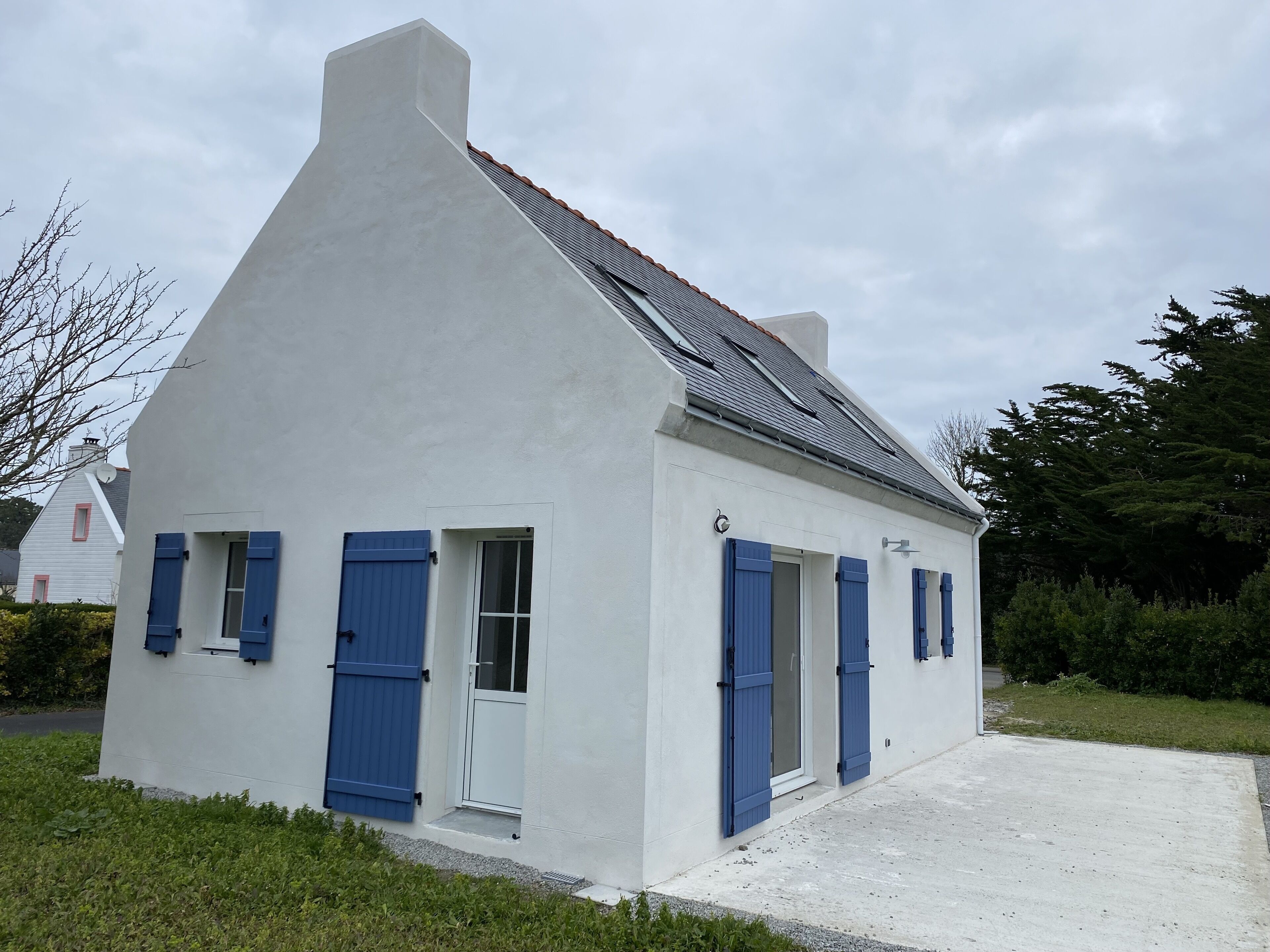 Un bâtiment blanc avec des volets bleus, un toit en pente et un petit porche.