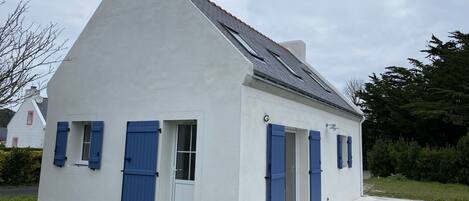 Un bâtiment blanc avec des volets bleus, un toit en pente et un petit porche.