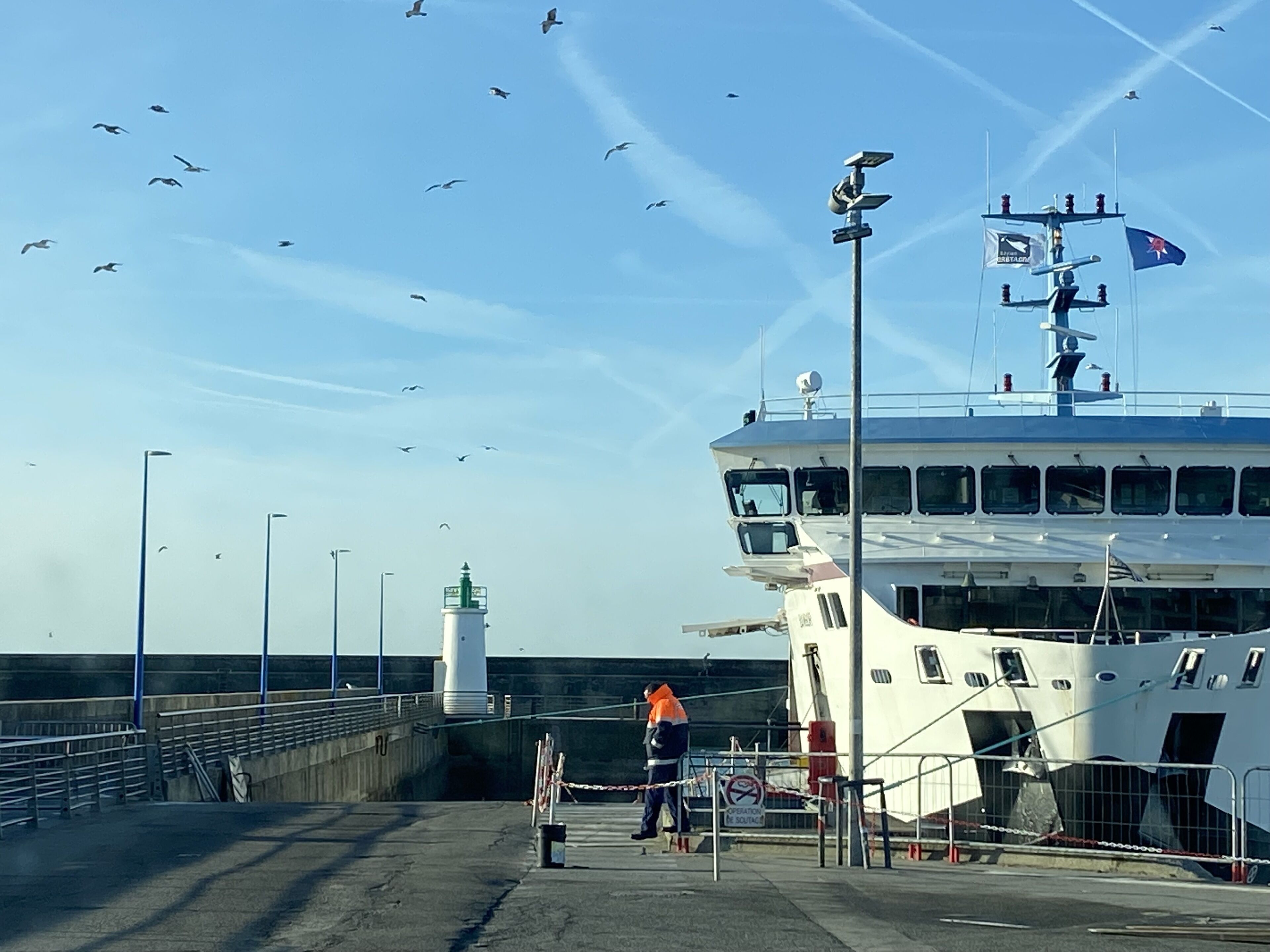 Un muelle de ferry con un transbordador blanco grande, un faro y una persona de pie cerca del muelle.
