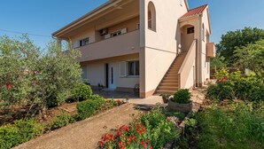Une maison à deux étages, avec un escalier menant à l’étage supérieur, entourée de verdure et d’un jardin.