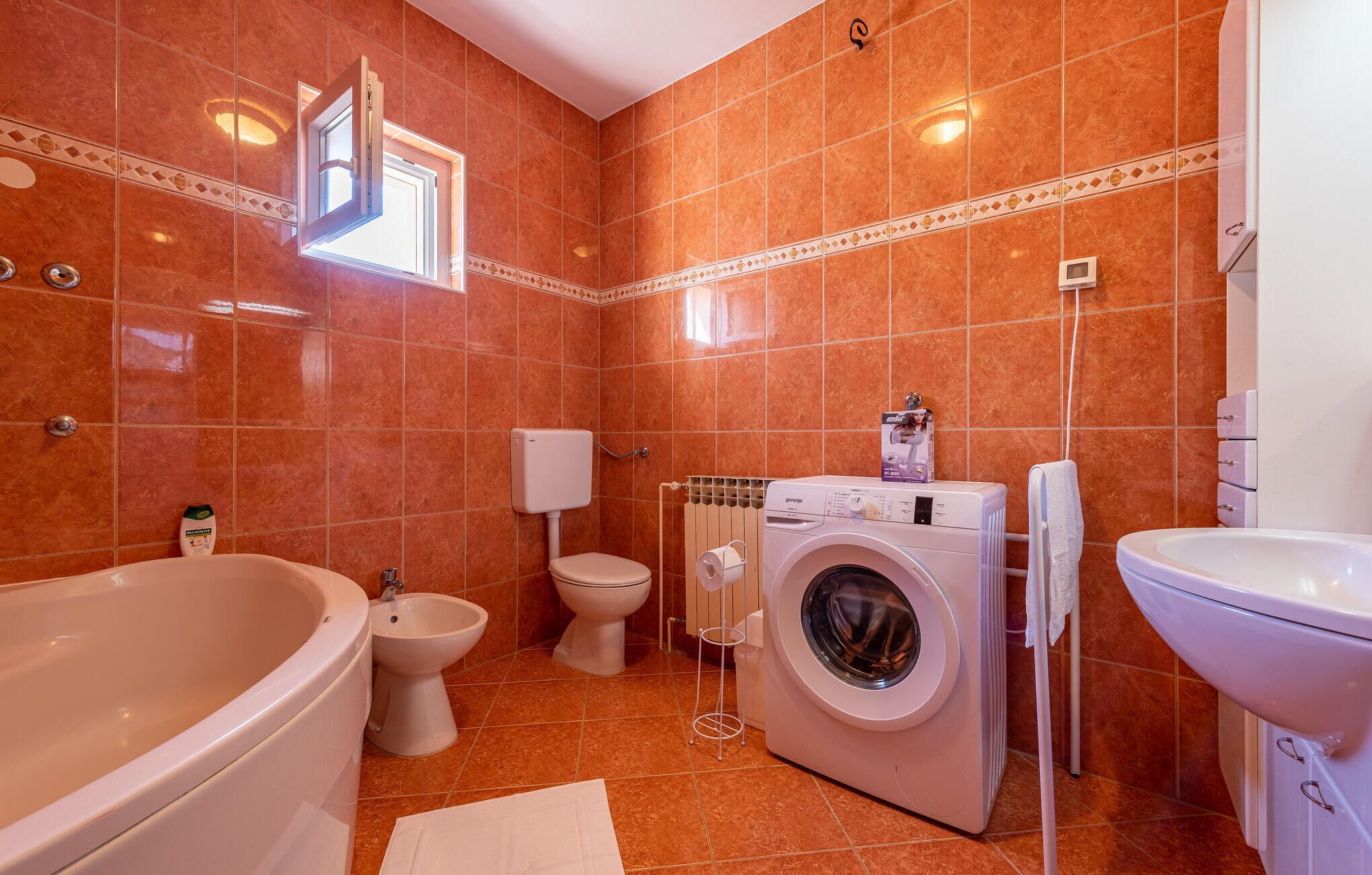 A bathroom with a bathtub, bidet, toilet, washing machine, and sink.