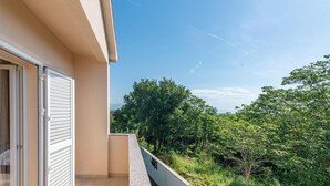 Un balcon donnant sur un paysage verdoyant et luxuriant, avec de nombreux arbres.