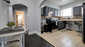 A modern kitchen with dark cabinets, a central island, and a dining area with a table and chairs. - Midtown Home Away From Home ShellCrestCorp 743 (Memphis)