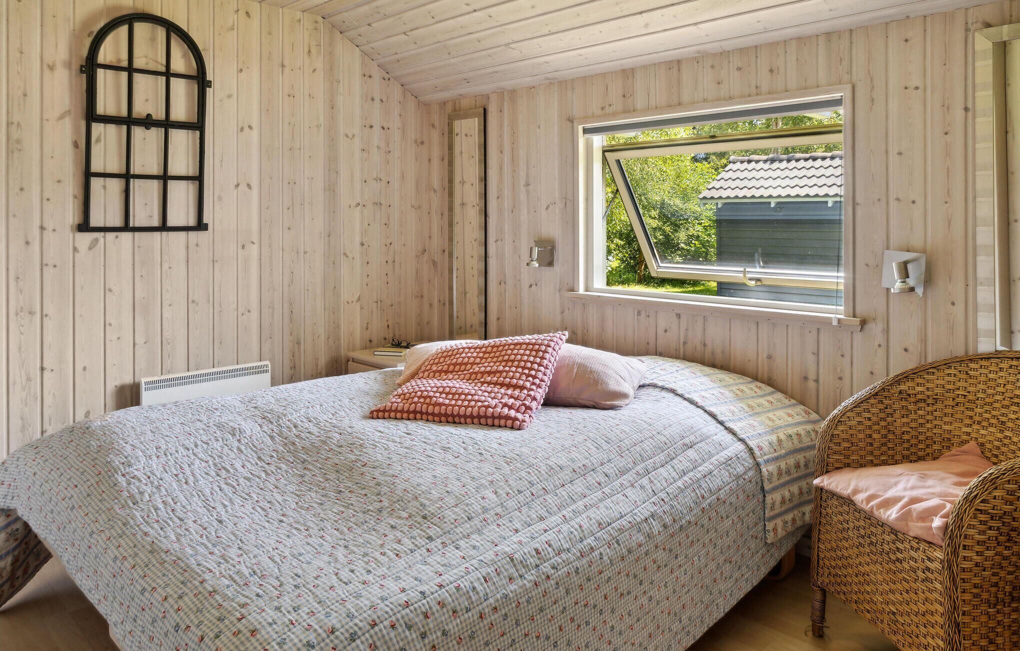 A bedroom with a bed, a window, a chair, and wooden walls.