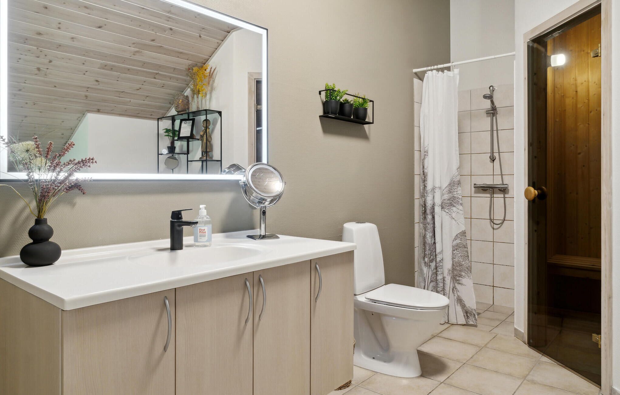 Ein Badezimmer mit weißem Waschbecken, Spiegel, Toilette, Dusche und einer Holztür.