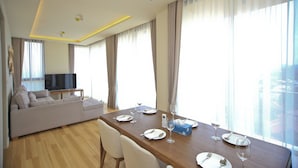 A modern living room with a sofa, a dining table set for two, and a television.
