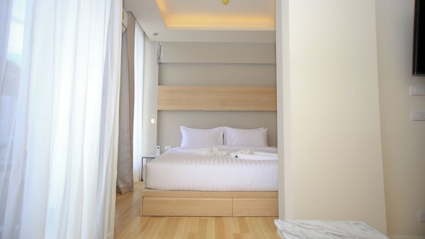 A modern hotel room with a bed, wooden floor, and a ceiling light.