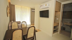 A dining area with a table and chairs, a television mounted on the wall, and an air conditioning unit.