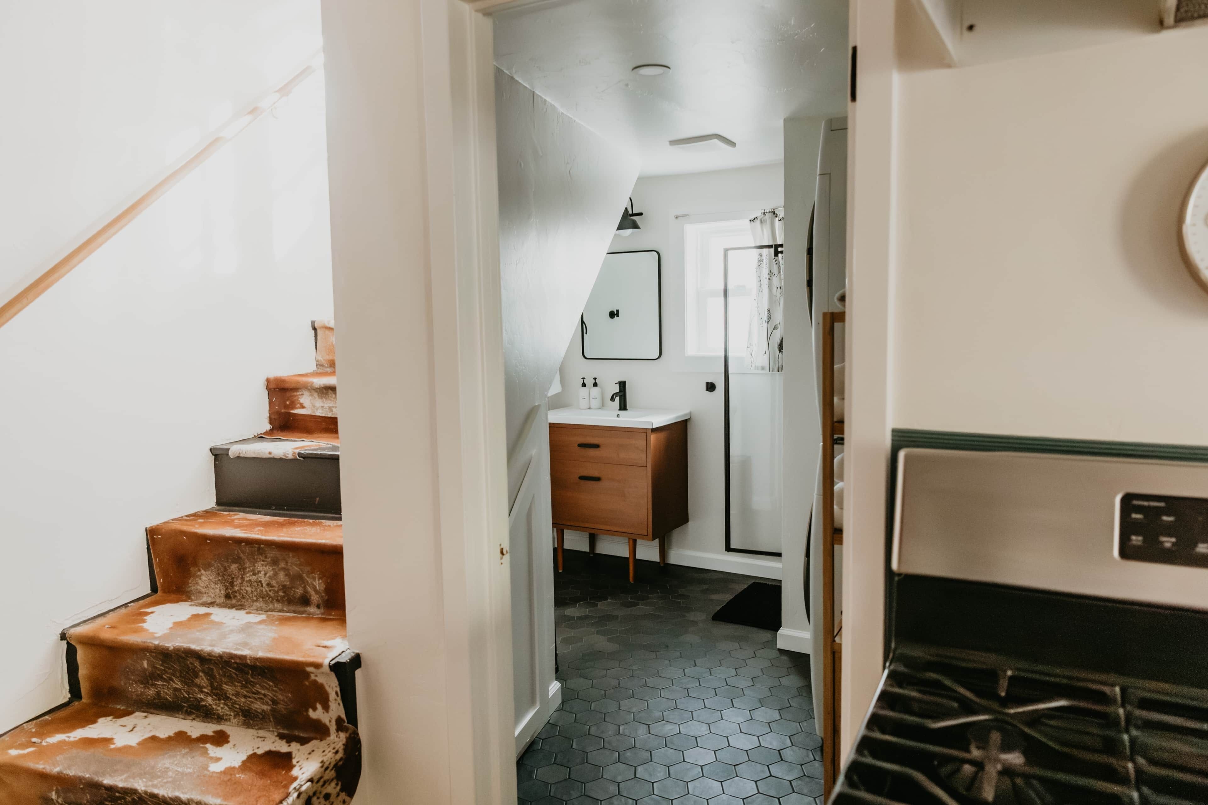 Un couloir étroit avec un escalier, une armoire en bois, un lavabo blanc et un miroir.