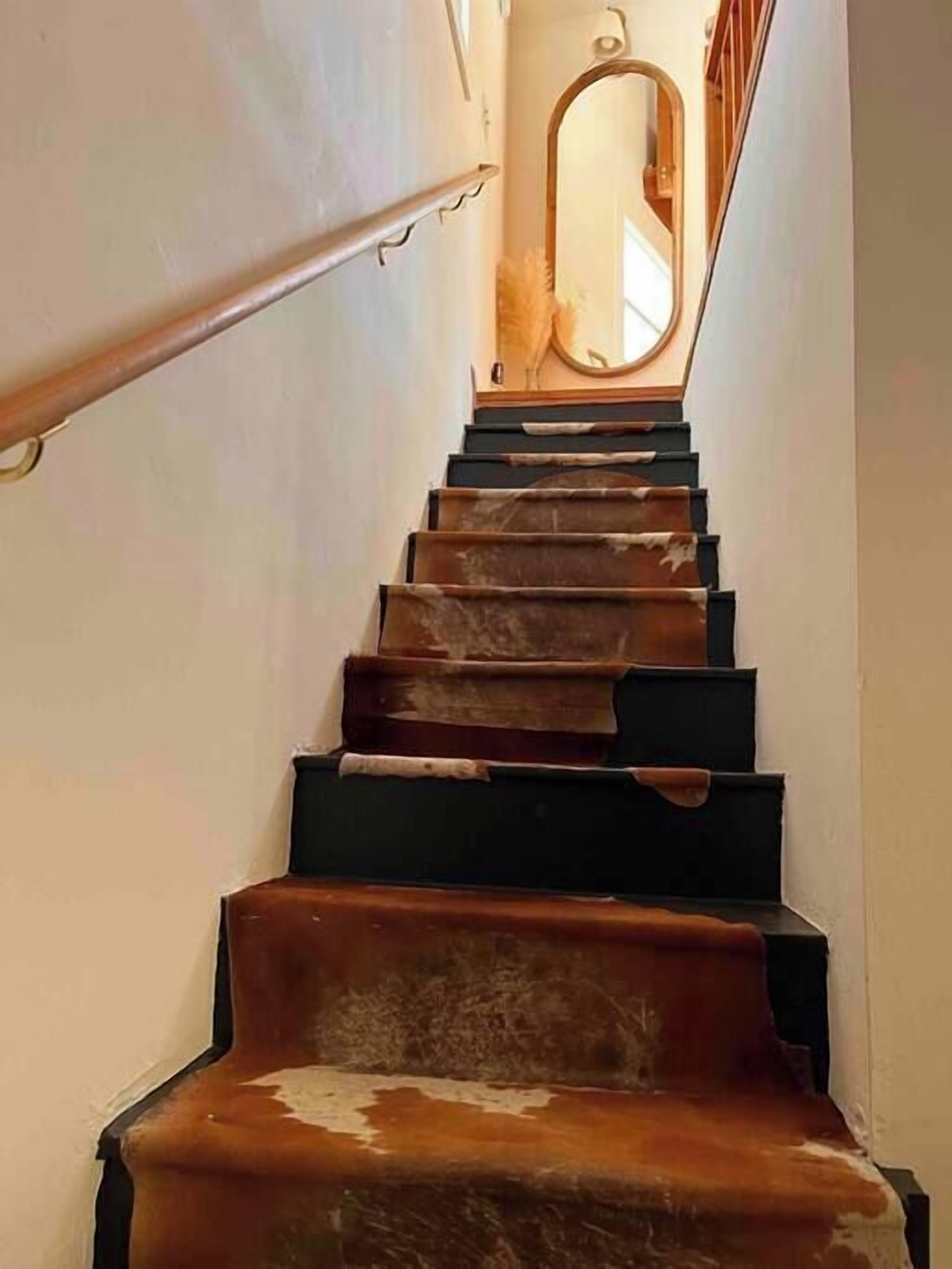 A staircase with a handrail on the left and a mirror on the wall at the top.