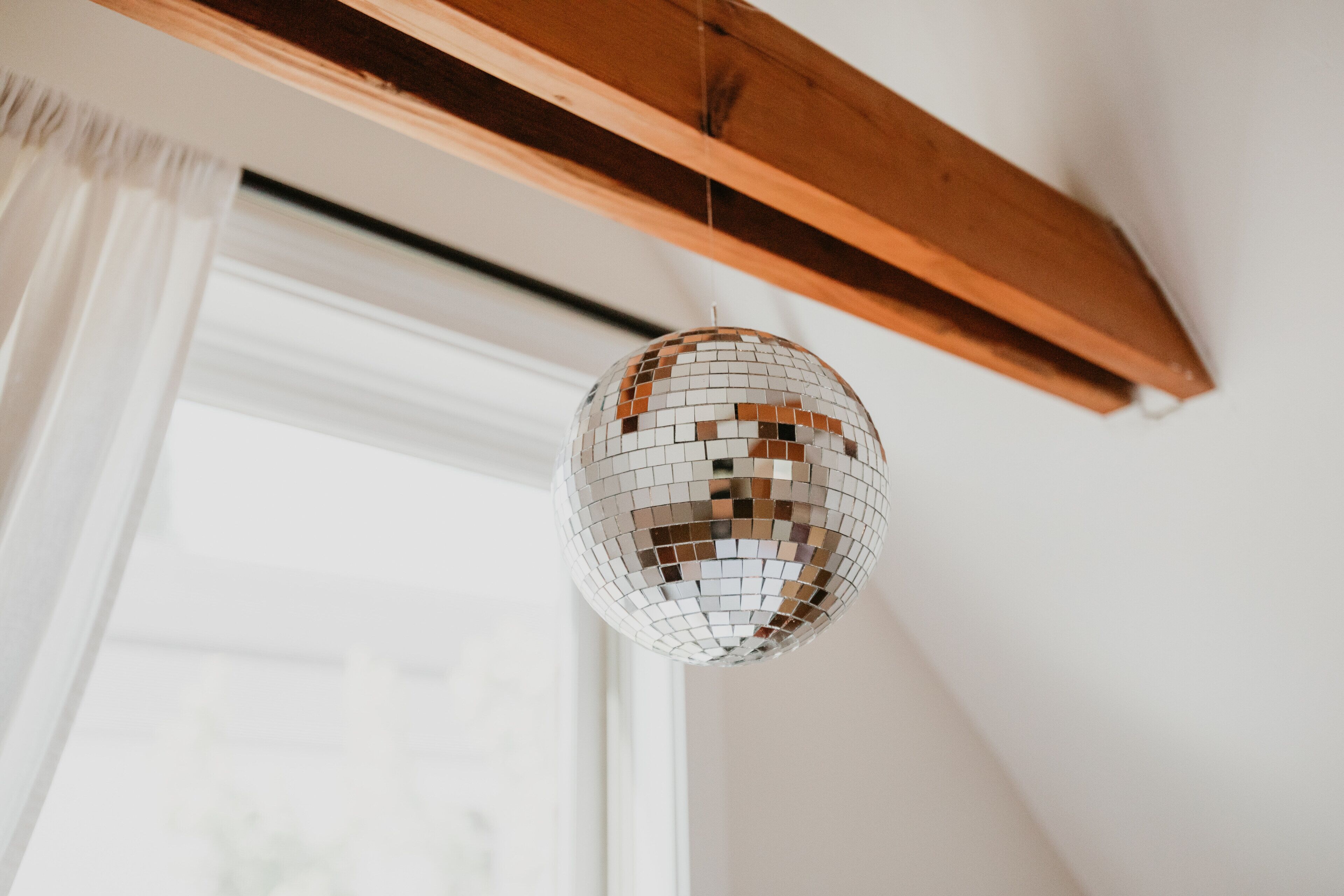 Une boule à facettes suspendue à une poutre en bois dans une pièce dotée d’une fenêtre.