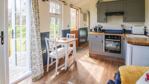 A cozy kitchen with wooden flooring, a dining table with chairs, a built-in oven, and a window with curtains.