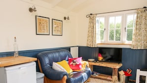 A cozy living room with a blue leather sofa, a wooden coffee table, a small TV, and a window with curtains.