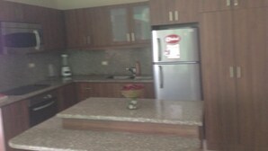 A kitchen with wooden cabinets, a stainless steel refrigerator, a microwave, and a granite countertop. - Departamento en Manta Frente al mar (Manta)