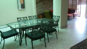 A dining area with a glass table and metal chairs, a brick wall, and a red sofa in the background. - Departamento en Manta Frente al mar (Manta)