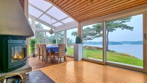 Una habitación acogedora con chimenea, una mesa de comedor y amplias ventanas con vistas a un lago.