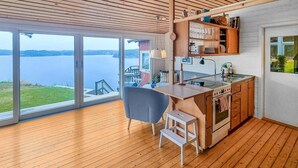 Cocina moderna con suelo de madera, una silla gris y vistas a un lago a través de puertas correderas grandes.