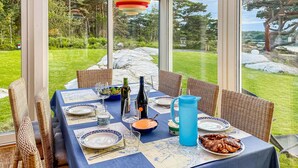 Un área de comedor al aire libre con sillas de mimbre, una mesa dispuesta con platos, vasos y una jarra azul.