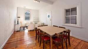 A dining room with a wooden table and chairs, a white wall, and a window. - Private Unit in Heritage Building in Fitzroy North (Fitzroy North)