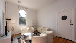 A modern living room with white furniture, a large window, and a checkered rug. - Private Unit in Heritage Building in Fitzroy North (Fitzroy North)