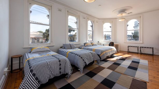 A room with three beds, large windows, and a checkered rug. - Private Unit in Heritage Building in Fitzroy North (Fitzroy North)