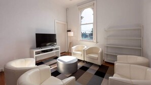 A modern living room with a flat-screen TV, white furniture, a patterned rug, and a large window with a view. - Private Unit in Heritage Building in Fitzroy North (Fitzroy North)