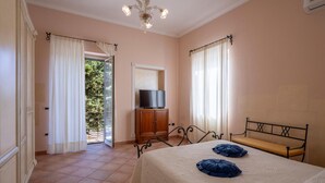 A bedroom with a bed, a television on a cabinet, and a balcony door.