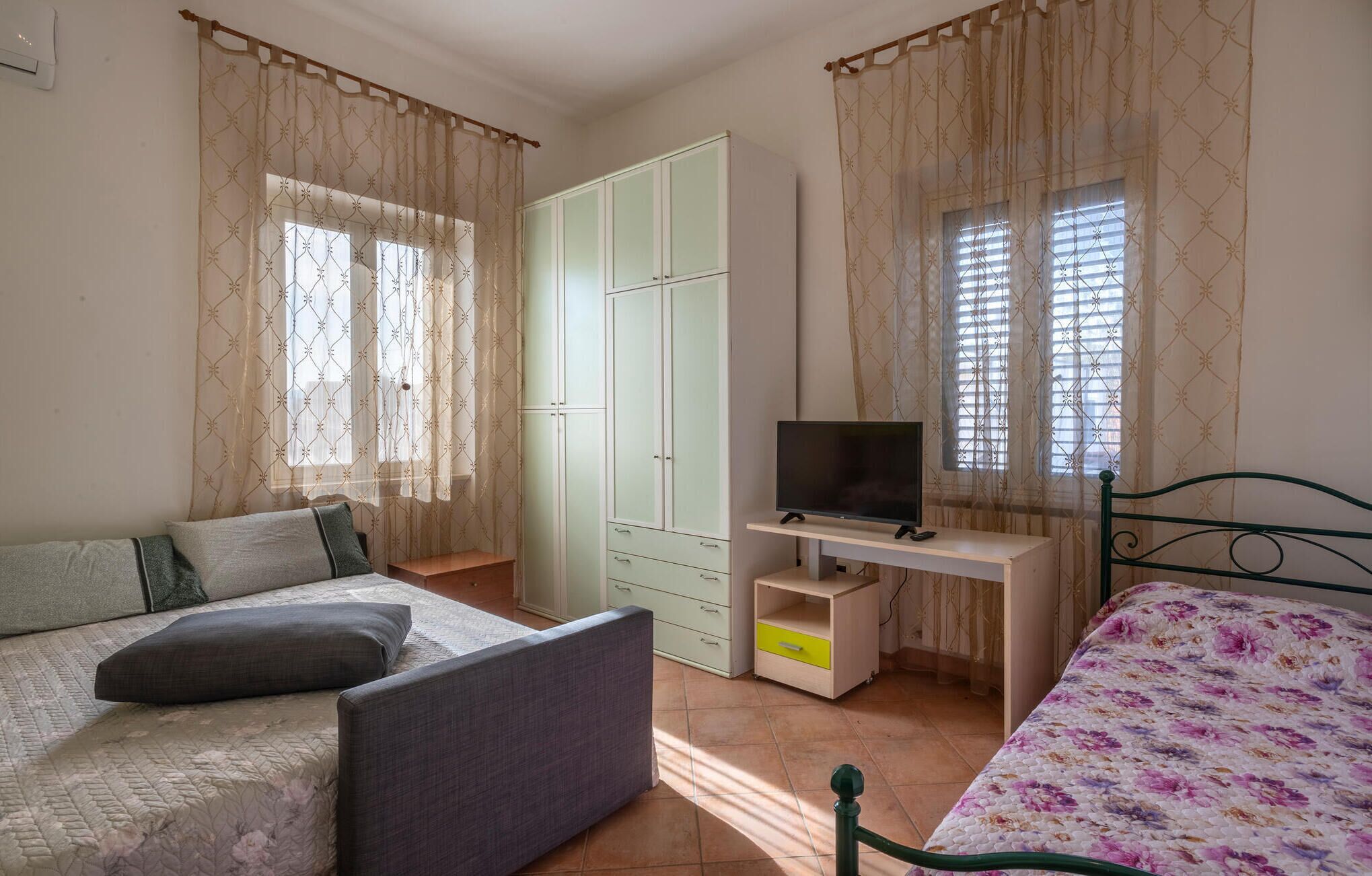 A bedroom with two beds, a TV, a wardrobe, and a desk.