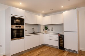 Une cuisine moderne avec des meubles blancs, un four encastré, un évier et un réfrigérateur.