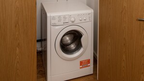 Une petite buanderie équipée d’un lave-linge à chargement frontal, d’un sèche-linge fixé au mur et d’un panneau de commande.